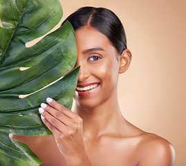 Image showing Portrait, facial and palm leaf with a model woman in studio on a beige background for natural skincare. Beauty, face and nature with an attractive young female posing for cosmetics or luxury wellness