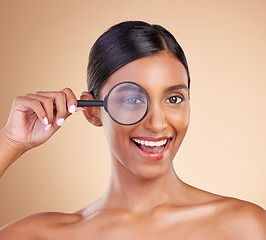 Image showing Portrait, beauty and magnifying glass with a model woman in studio on a beige background searching for skincare. Face, eye and investigation with an excited young female looking for luxury cosmetics