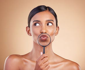 Image showing Mouth, lips or woman with magnifying glass in studio on beige background searching for facial beauty. Face, headshot or young Indian girl looking for luxury self care cosmetics, lipstick or makeup