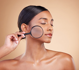 Image showing Skincare, model face or woman with magnifying glass in studio on beige background searching for beauty. Facial, eyes closed or young Indian girl looking for luxury self care cosmetics or makeup