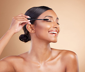 Image showing Makeup, happy and woman with mascara for eyelashes isolated on a studio background. Smile, cosmetology and Indian girl with a brush for applying cosmetics, pomade product or treatment to lashes