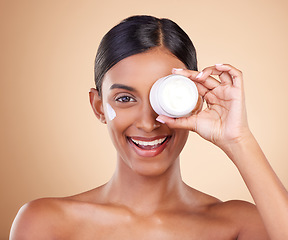 Image showing Beauty, face cream and portrait of a woman in studio for skincare, dermatology and cosmetics. Happy Indian female model with smile and lotion on hand for self care moisture facial on brown background