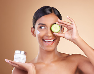 Image showing Beauty, skincare and Indian woman with cucumber, cream and dermatology against a brown studio background. Female, cosmetics and happy lady with natural care, lotion and healthy detox with grooming