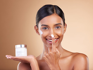 Image showing Portrait, product and nose with a model woman in studio on a beige background to apply facial lotion. Face, beauty and skincare with an attractive young female applying moisturizer to her skin