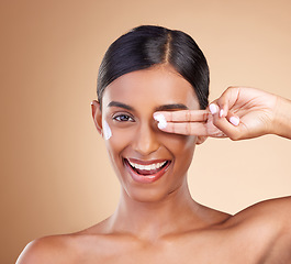 Image showing Beauty, face cream and portrait of a woman in studio for skincare, dermatology and cosmetics. Happy Indian female model with smile and lotion on hand for self care moisture facial on brown background