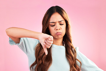 Image showing Unhappy, thumb down and sad woman in a studio with an upset, moody or disappointed face. Loser, rejection and young female model posing with a disagreement hand gesture isolated by a pink background.