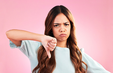 Image showing Upset, thumbs down and portrait of a female in a studio with a sad, moody or disappointed face. Loser, unhappy and young woman model posing with a angry hand gesture isolated by a pink background.