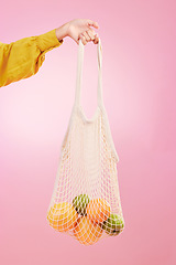 Image showing Hand, shopping and bag with fruit in studio by pink background for diet, health and deal in recycle material. Grocery discount, fruits or vegetables from store for food, sustainability and lifestyle