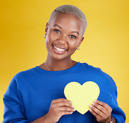 Image showing Paper heart, portrait and happy black woman in studio, background and color backdrop. Smile, female model and yellow shape for love, wellness and caring support of peace, romance and sign of kindness