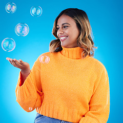 Image showing Happy, holding and bubble with indian woman in studio for soap, positive and satisfaction. Magic, creative and smile with female isolated on blue background for bright, cute and entertainment