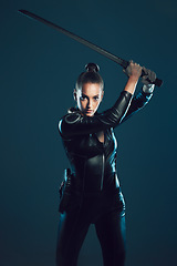 Image showing Woman, warrior and vigilante in cosplay with sword ready for battle, war or game against a dark studio background. Female in black costume or hero with guns and blade for halloween or super power