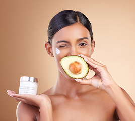 Image showing Beauty, avocado and face cream woman portrait in studio for cosmetics, skin glow and natural product. Indian female model wink on beige background for skincare, facial self care and organic container