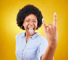 Image showing Rock hand, metal and black woman portrait in studio with tongue out for punk music. Happiness, freedom and cool young female with isolated yellow background feeling edgy with rocker hands sign