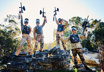 Image showing Team, paintball and portrait in celebration for winning, victory or achievement standing on tires together in nature. Group of people enjoying win, success or teamwork with guns in the air for sports