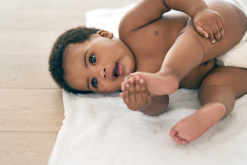 Image showing Baby, infant and black child lying down newborn relax in a home, nursery or house floor with a diaper playing with feet. Cute, adorable and innocent little kid with happiness in development