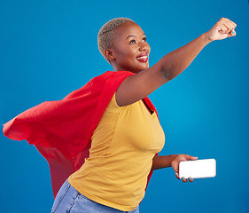 Image showing Superhero, mockup and phone with black woman in studio for flying, power and deal. Mobile, strong and communication with female in red cape costume on blue background for technology, digital and 5g