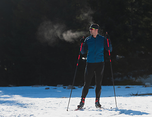 Image showing Portrait handsome male athlete with cross country skis, taking fresh breath and having break after hard workout training in a snowy forest. Healthy winter lifestyle concept