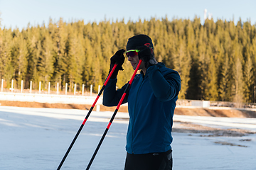 Image showing Handsome male athlete with cross country skis preparing equipment for training in a snowy forest. Checking smartwatch. Healthy winter lifestyle.