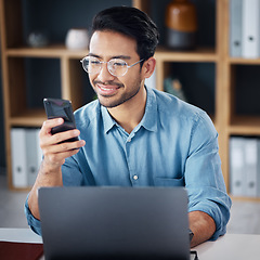 Image showing Happy asian man, phone and laptop for social media, communication or networking at office desk. Male creative designer smiling with smartphone by computer for browsing, research or planning startup