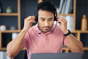 Image showing Serious asian man, call center and headset on laptop for consulting, customer service or support at office desk. Focused male consultant putting on headphones by computer for telemarketing or advice