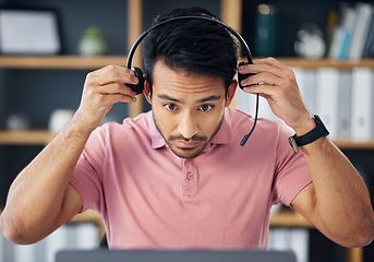 Image showing Asian man, call center and headset on laptop ready for consulting, customer service or support at office desk. Serious male consultant putting on headphones by computer for telemarketing or advice