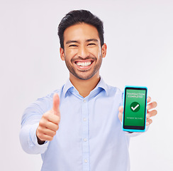 Image showing Asian man, portrait and phone with thumbs up for transaction approval against a white studio background. Happy male smile showing thumb emoji, yes sign or like for electronic purchase on smartphone