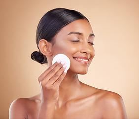 Image showing Smile, makeup or happy woman with cotton pad in studio isolated on beige background for facial skincare. Glowing natural beauty or beautiful young Indian girl cleaning for self care or face wipes