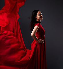 Image showing Happy woman, art and fashion, red fabric on dark background with beauty and aesthetic movement. Flowing silk, fantasy and artistic model with smile in creative designer dress in studio with motion.