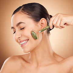 Image showing Skincare, jade roller and happy woman in studio for beauty, wellness and anti aging against brown background. Facial, skin and girl relax with massaging tool, facelift and lymphatic drainage isolated