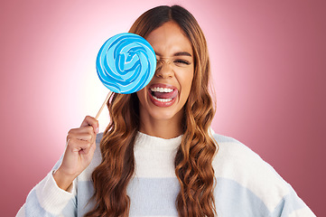 Image showing Portrait, funny face and lollipop with a woman in studio on a pink background holding giant candy. Comic, comedy and sweet with a playful young female feeling silly while eating a blue sugar treat