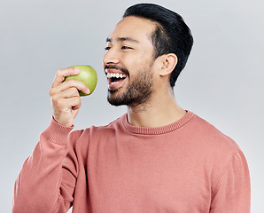 Image showing Healthy, happy and an Asian man eating an apple isolated on a white background in a studio. Smile, food and a Chinese guy taking a bite from a fruit for nutrition, diet or hungry on a backdrop