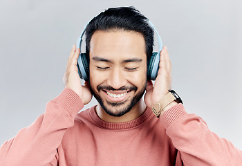 Image showing Happy, music and Asian man with headphones, streaming and cheerful on a grey studio background. Japan, male and confident guy with headset, listening to audio and sounds for peace, smile and wellness