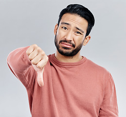 Image showing Sad, disappointment and portrait of an Asian man with a thumbs down isolated on a studio background. Review, unhappy and a Chinese guy with a hand sign for a problem, mistake and dislike emoji