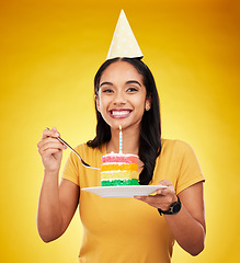Image showing Woman is eating birthday cake, celebration and happy in portrait, rainbow dessert and candle on yellow background. Celebrate, festive and young female, excited for sweet treat and party hat in studio