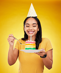 Image showing Woman is eating cake, birthday celebration and happy in portrait, rainbow dessert and candle on yellow background. Celebrate, festive and young female, excited for sweet treat and party hat in studio