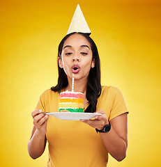 Image showing Woman, birthday cake and celebration, blow out candle with rainbow dessert isolated on yellow background. Celebrate, festive and young female, making a wish with sweet treat and party hat in studio