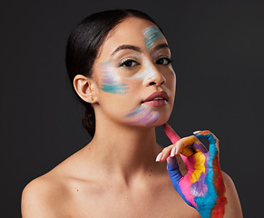 Image showing Woman, beauty and portrait with rainbow hand paint art on face in studio with glow. Creative skin and makeup on female aesthetic model serious on gray background for lgbtq color inspiration on hands