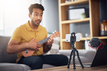 Image showing Podcast microphone, phone and guitar with a man online to coach during live streaming lesson. Asian male influencer on home sofa with a ukulele as content creator teaching music on education blog