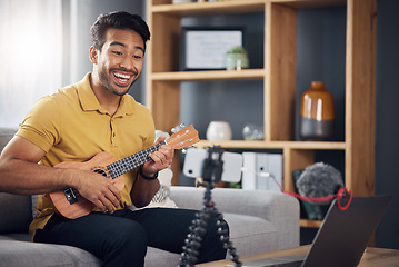 Image showing Phone, guitar tutorial and man with a smile online to coach during live streaming lesson. Asian male influencer happy on home sofa with a ukulele as content creator teaching music on education blog