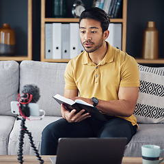 Image showing Podcast, bible and man reading with phone and microphone online while live streaming. Asian male on home sofa with Christian religion book as blog content creator or influencer teaching or studying