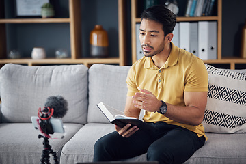 Image showing Podcast, bible study and phone with a man online to preach or reading while live streaming. Asian male on home sofa with Christian scripture or book as content creator teaching on education religion