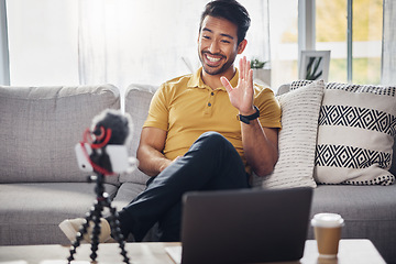 Image showing Laptop, phone and content creation, Indian man on sofa, webinar recording and live streaming in home. Internet, webcam and online influencer with smile, wave and equipment for social media channel.