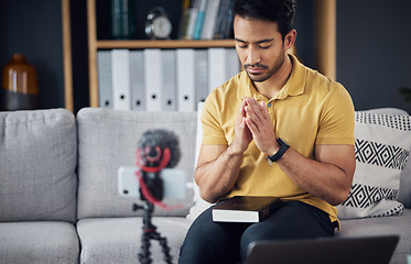 Image showing Podcast, bible and man pray with a phone and microphone online while live streaming. Asian male on home sofa to pray with hands and Christian religion book as blog content creator or influencer