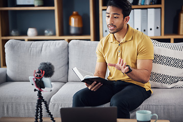 Image showing Book, bible study and phone with a man online to preach or reading while live streaming. Asian male on home sofa talking Christian scripture as podcast content creator teaching education on religion