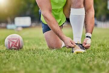 Image showing Rugby ball, hands and tying shoe lace on grass field getting ready for sports match or game outdoors. Hand of sporty man tie shoes in preparation for sport, performance or motivation in park