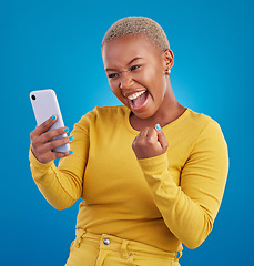 Image showing Black woman, phone and fist celebration in studio, blue background and winning online prize. Happy female model celebrate mobile promotion, bonus and excited for deal, success and competition winner