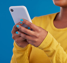 Image showing Phone, typing and closeup of hands of woman in studio for social media, text message and browse website. Communication, technology and girl on internet, network and chat online on blue background