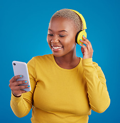 Image showing Search, phone and music with black woman in studio for streaming, multimedia and browsing. Gen z, smile and audio with female and headphones on blue background for listening, online radio and songs