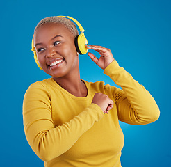 Image showing Black woman, headphones and listening to music with a smile in studio while happy streaming audio. African female model on a blue background to listen to radio, podcast or sound with a positive mood