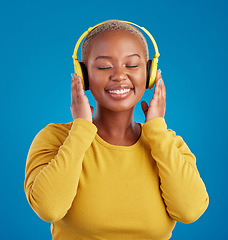 Image showing Black woman, face and headphones, listening to music with rhythm and fun with freedom on blue background. Happy female with smile, streaming radio or podcast with peace and eyes closed in studio